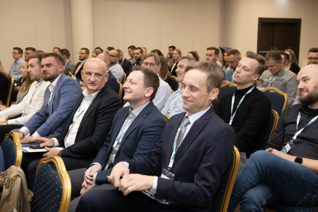 Participants of an international conference, dressed in business casual, sitting in rows in a conference room and listening to a speaker