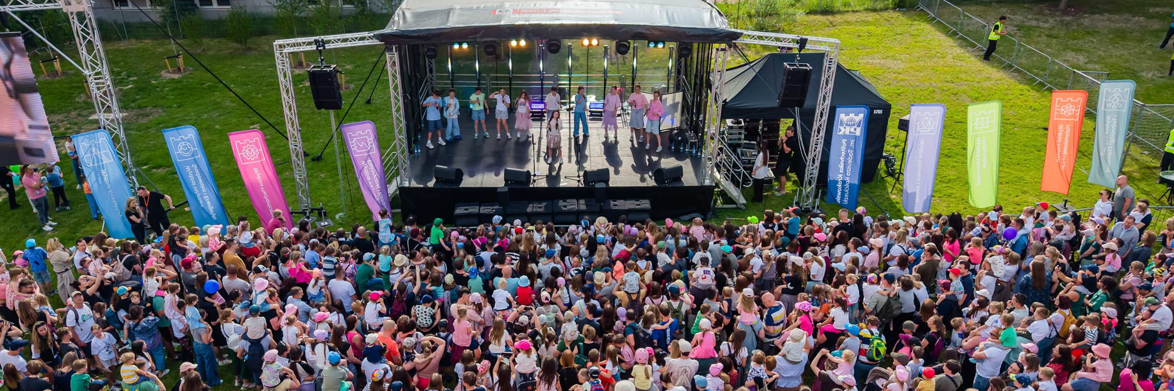 Słoneczny dzień, koncert plenerowy. Przed sceną tłum ludzi. Widok z lotu ptaka