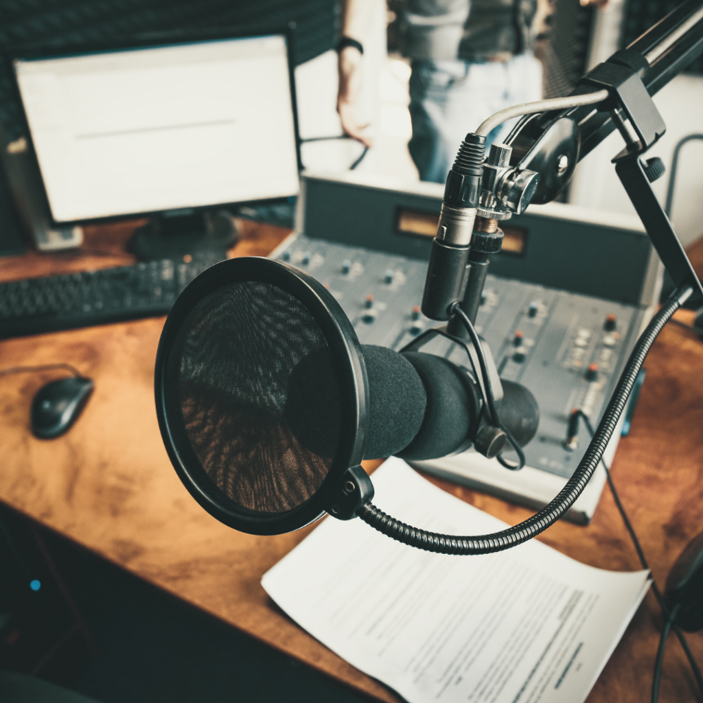 Studio nagraniowe, radiowe urządzone w ciepłym, przytulnym stylu. Drewno, ciepłe kolory. Na stole konsola i monitor. Na pierwszym planie mikrofon