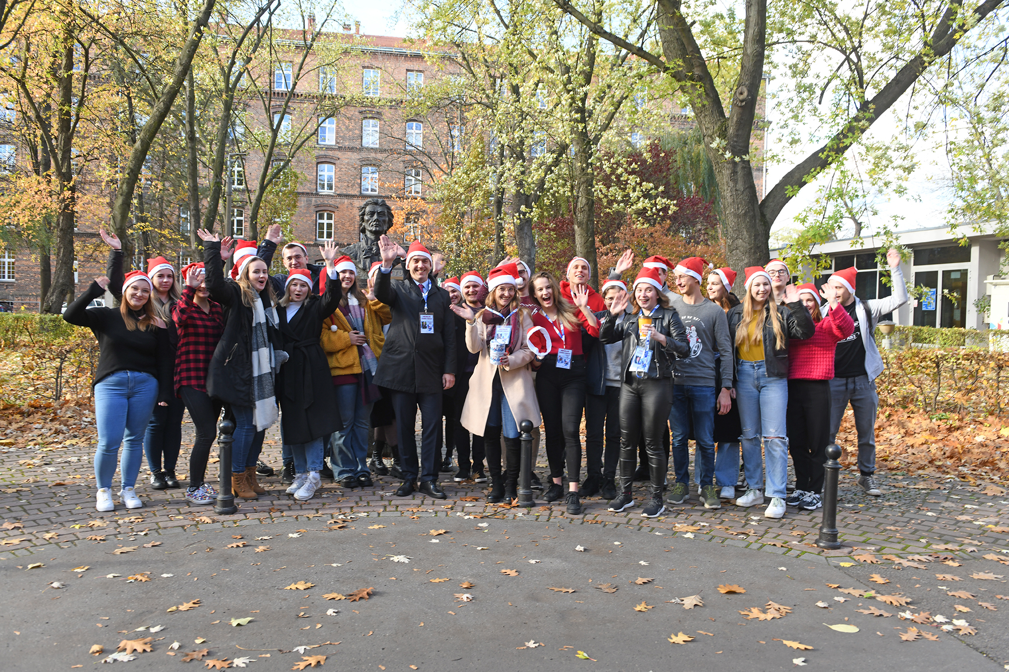 Grupa studentek i studentów w czapkach mikołajkowych pozuje do wspólnego zdjęcia pod popiersiem Tadeusza Kościuszki na Dziedzińcu uczelni. Wśród młodzieży jest też Rektor Andrzej Szarata.
